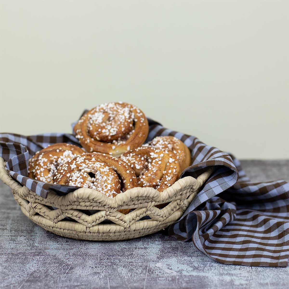 Kanelbullar som ligger i en naturfägad korg med en blåbrun kökshandduk