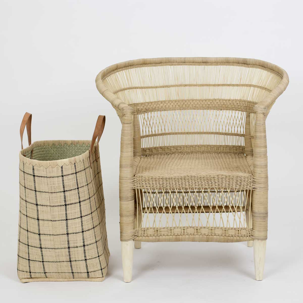En RAFFIA Tvättkorg i natur och svart står bredvid en rottingfåtölj