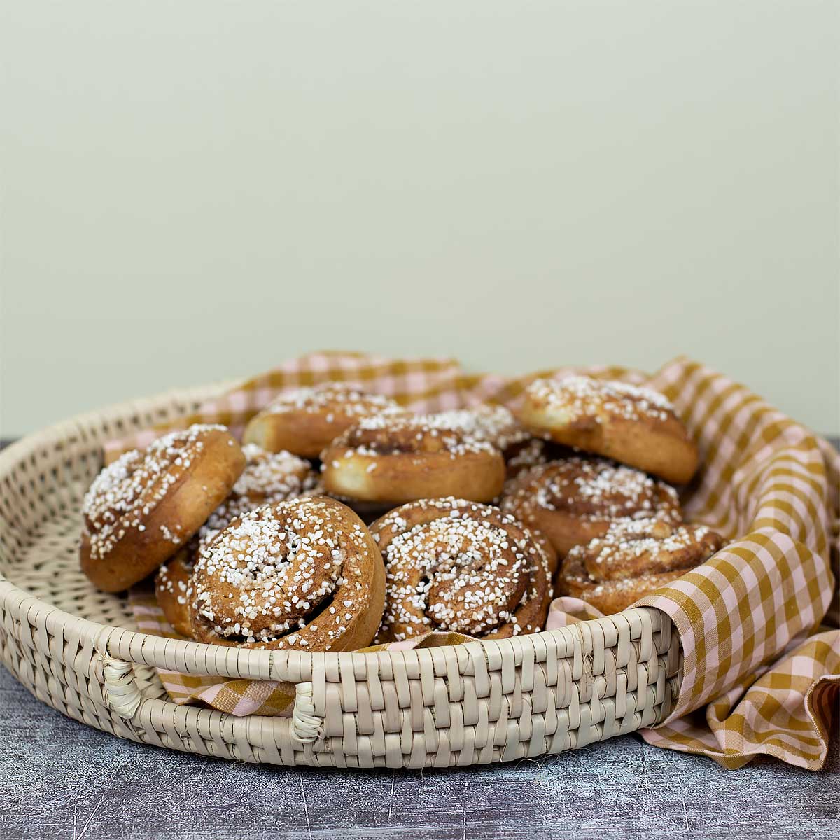 Naturfärgad bricka med handtag där det ligger kanelbullar och en vit-orange kökshandduk